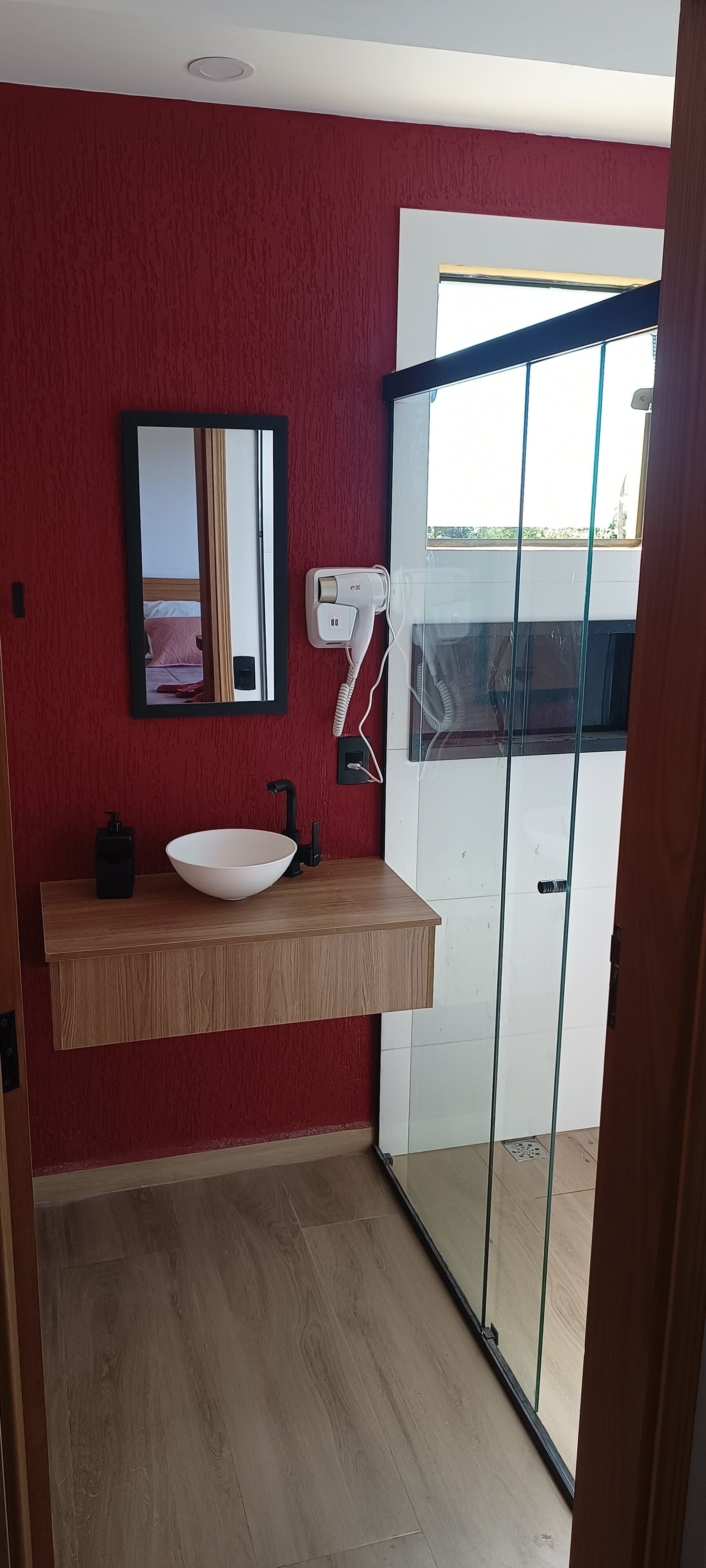A bathroom with a wooden vanity, a white sink, a mirror, and a glass shower door.