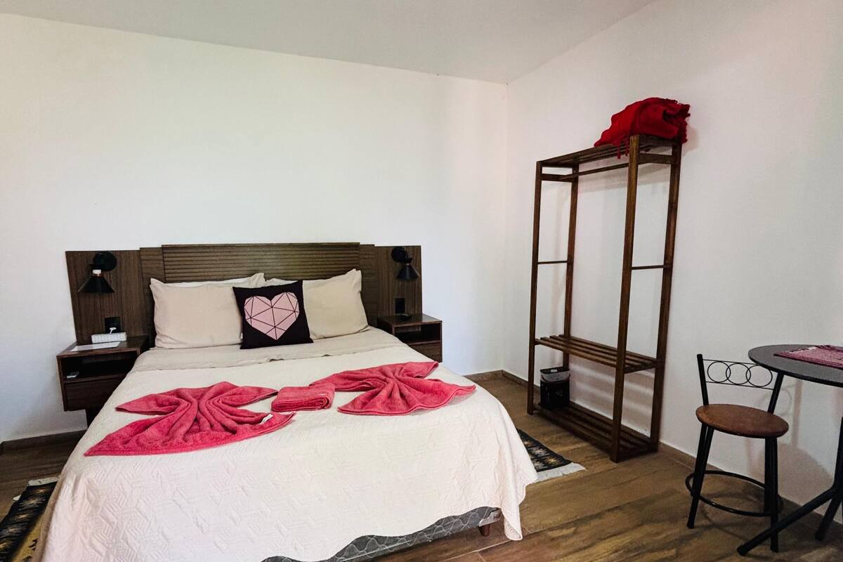 Een keurig opgemaakt slaapkamer met een bed, nachtkastjes, een klein tafeltje en een stoel.