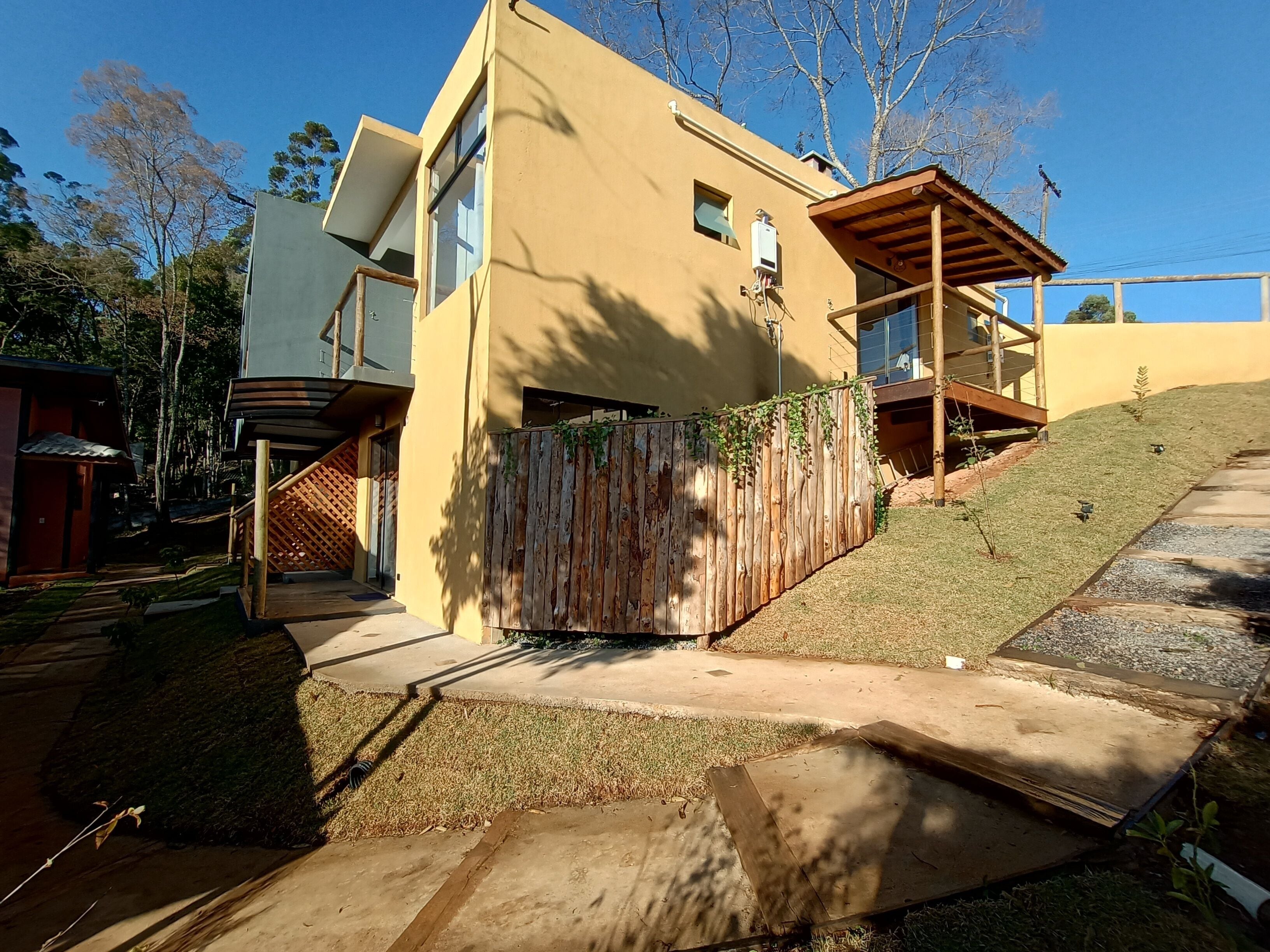 Una casa moderna de dos pisos con una terraza de madera, un espacio exterior cubierto y un pequeño jardín.