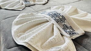 Una cama bien hecha con toallas blancas y estampadas, una lámpara de noche y vistas a la vegetación a través de una ventana.
