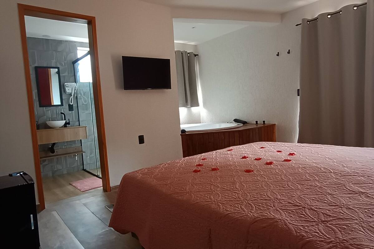 Een slaapkamer met een bed, een televisie, een badkamer zichtbaar door een geopende deur en een houten stoel.