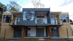Una casa moderna de dos pisos con balcón, ventanas amplias y un pequeño jardín delantero.