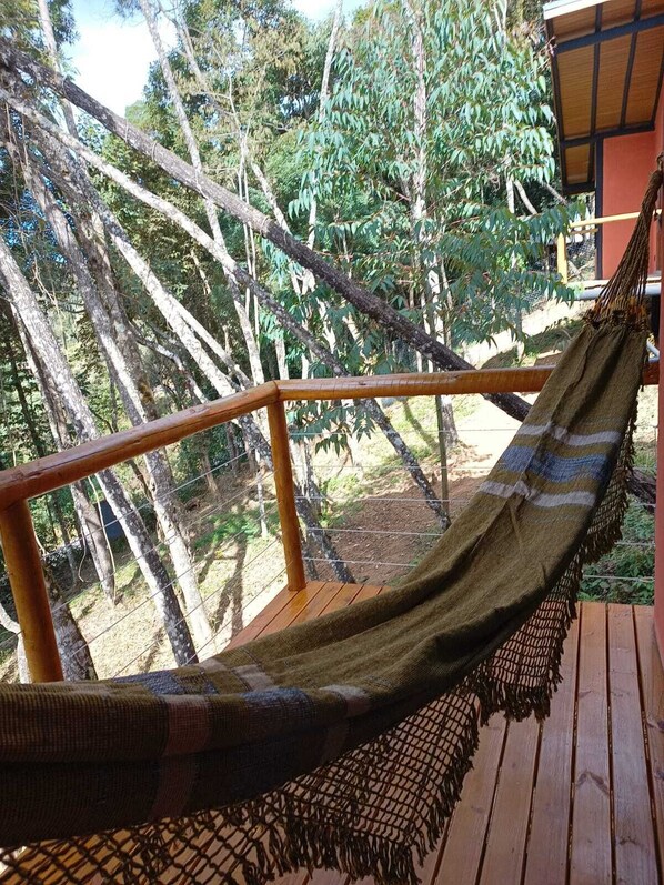 Una hamaca en una terraza de madera con vista a árboles y un edificio al fondo.