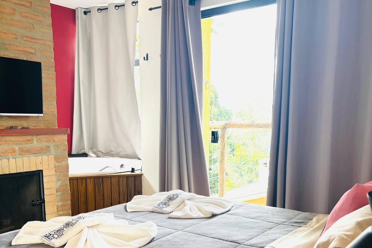 Hotelkamer met een bed, een flatscreen televisie bevestigd aan een bakstenen muur, een open haard en een raam met gordijnen.