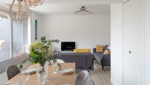 Ein modernes Wohnzimmer mit einem grauen Sofa, einem Holzesstisch gedeckt mit Tellern und Gläsern sowie einem Fernseher auf einem Lowboard.