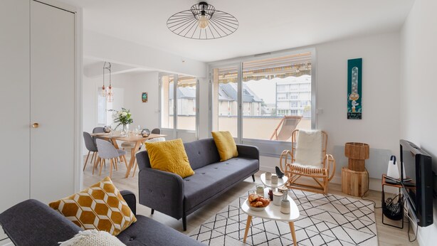 Ein modernes Wohnzimmer mit einem grauen Sofa, einem Esstisch und einem Fernseher.