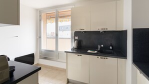 Eine moderne Küche mit schwarzem Arbeitsplatz, weißen Schränken und einem großen Fenster mit Blick auf Gebäude.