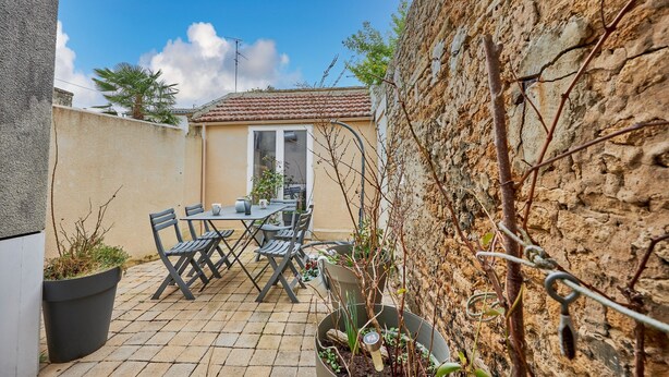 Une terrasse avec une table et des chaises, des plantes en pot et un mur en pierre.