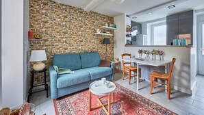 Un salon avec un canapé bleu, une petite table ronde, un tapis à motifs et un mur en briques.