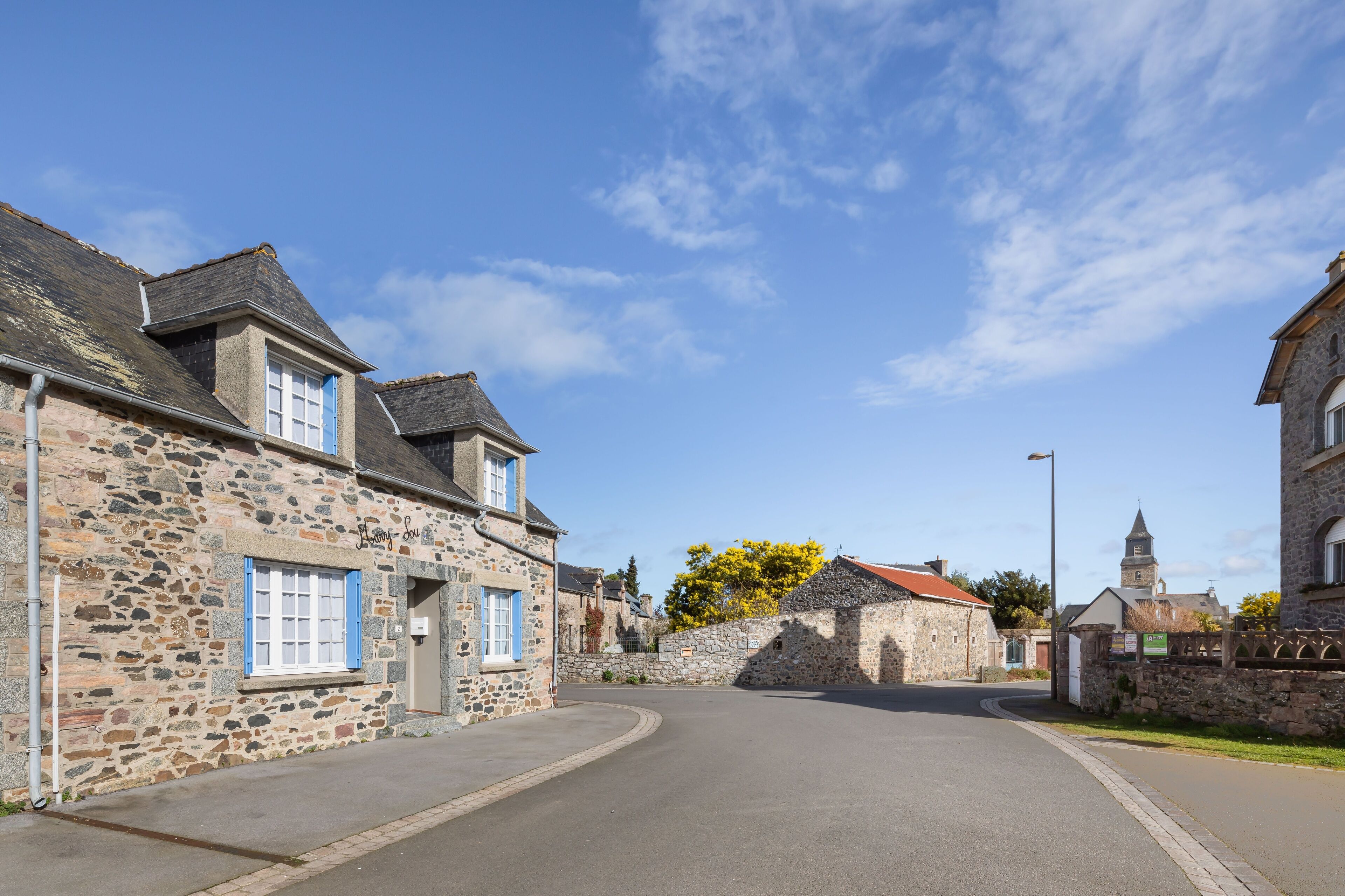 A stone building with a curved road, a church in the distance, and a clear blue sky.