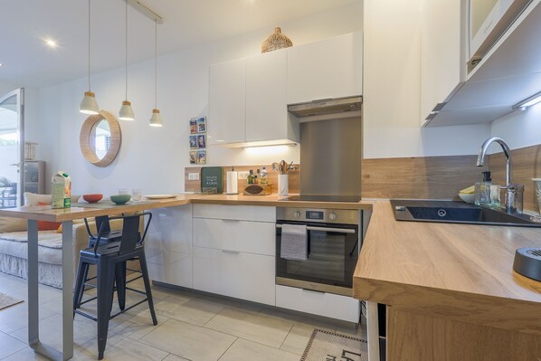 A modern kitchen with a wooden countertop, built-in oven, stainless steel sink, and pendant lighting.