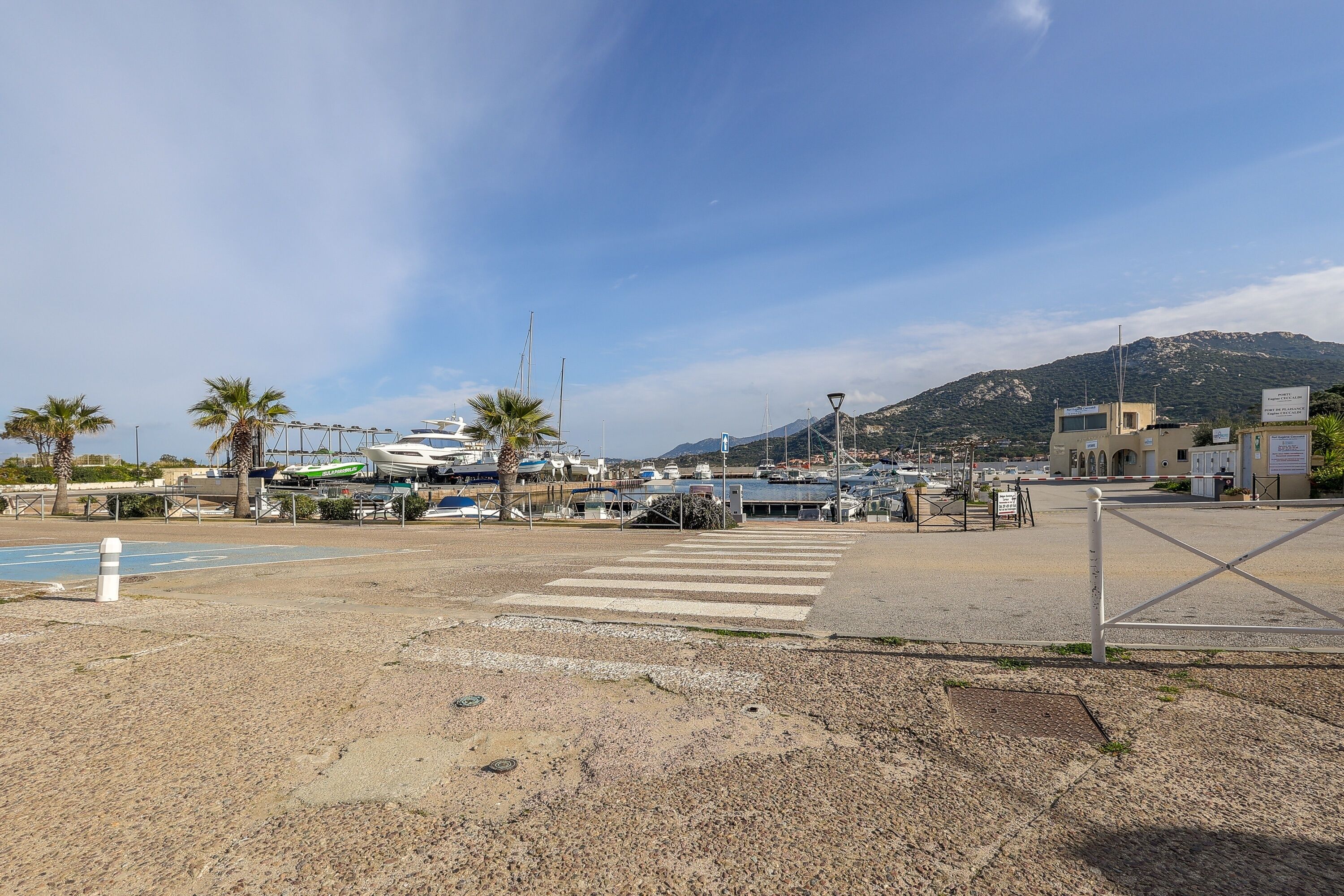 A marina with boats docked, a pedestrian crossing, and a mountain in the background.
