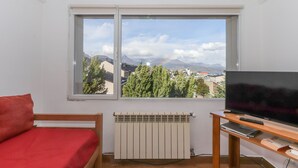 A room with a bed, a TV on a stand, a radiator, and a window with a mountain view. - Mystico (Ushuaia)