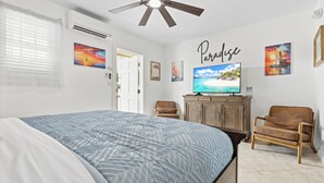 A bedroom with a bed, a ceiling fan, a TV, a wooden cabinet, and two chairs. - Prime Downtown Key West Spot - The Cozy Little Cottage! (Key West)