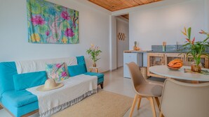 Ein modernes Wohnzimmer mit einem türkisfarbenen Sofa, einem Esstisch mit Stühlen und einer Küche im Hintergrund.