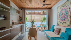 Ein modernes Wohnzimmer mit Holzboden, einem smaragdgrünen Sofa, einem Esstisch mit Stühlen und einer Küchenzeile inklusive Toaster und Topfpflanzen.