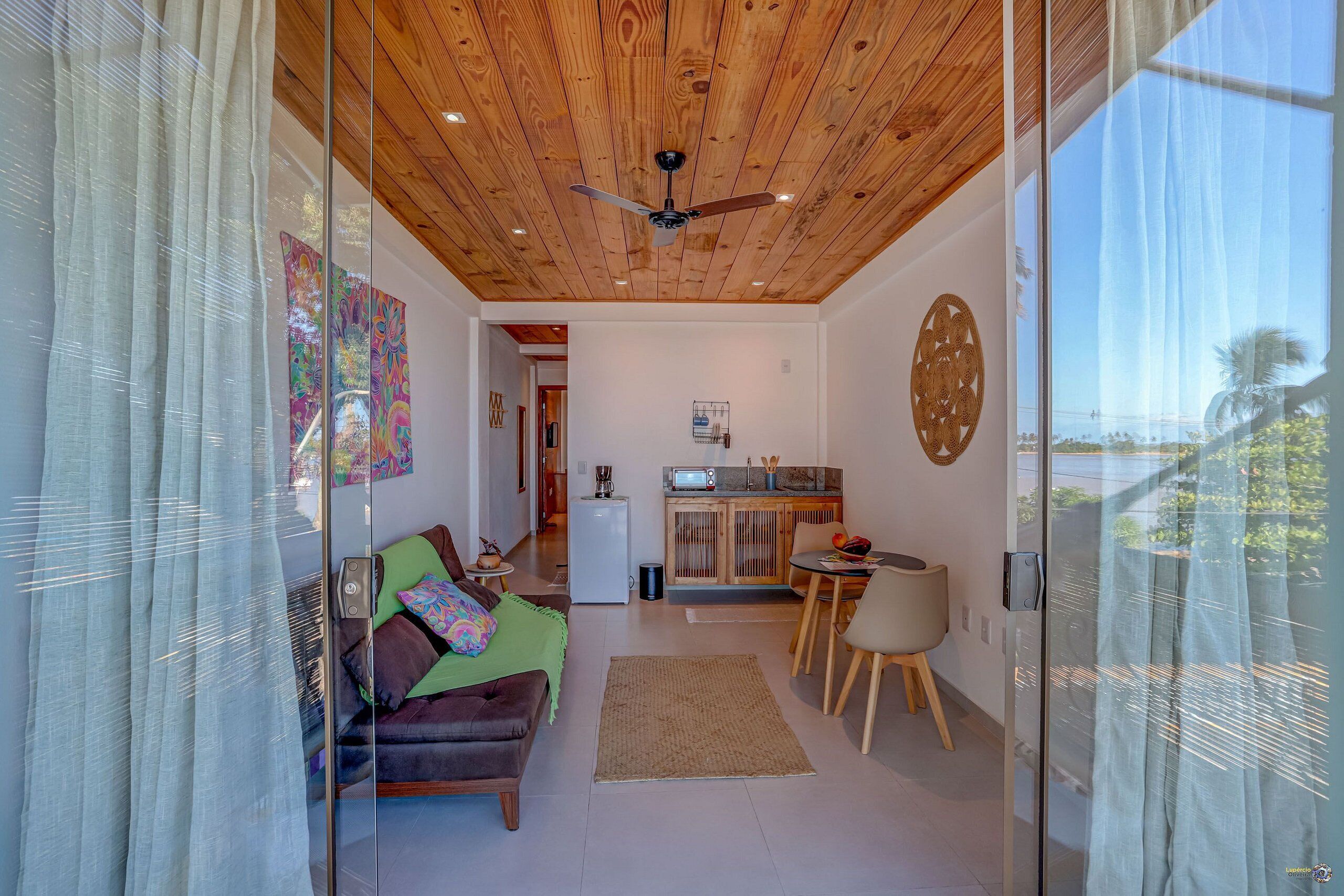 A modern living room with a wooden ceiling, a sofa, a coffee table, and a kitchen area with a refrigerator and microwave.