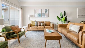 A living room with a green armchair, a brown leather sofa, and a wooden coffee table. There is a large plant and abstract wall art.