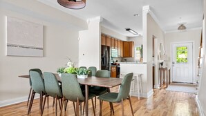 A dining area with a wooden table and green chairs, a kitchen with wooden cabinets, and a white door with a window.