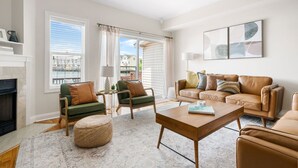A living room with a fireplace, a sofa set, a coffee table, and a view of the outside.