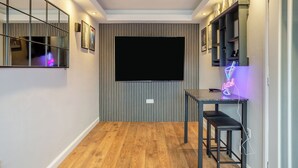 Un soggiorno moderno con una TV a schermo piatto montata su una parete a righe, un pavimento in legno e un neon su un tavolo.