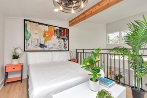 Ein Schlafzimmer mit einem großen Bett, einem Nachttisch mit Pflanze, einem Gemälde an der Wand und einem Balkon mit Pflanzen.