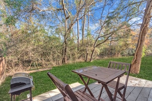 Eine Terrasse mit Grill, Holztisch und Stühlen.