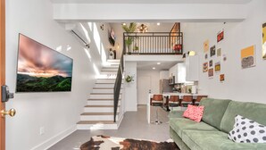 Ein modernes Interieur mit einer Treppe zu einem Schlafzimmer-Bereich, einem grünen Sofa und einem Essbereich.