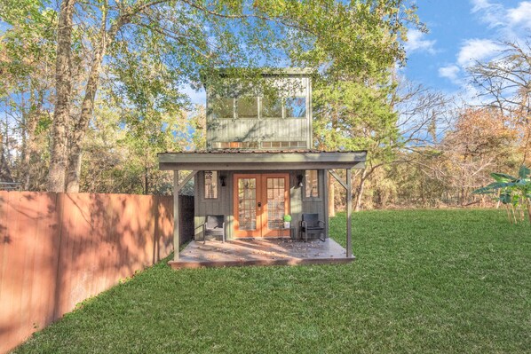 A two-story house with a covered porch, a fenced yard, and trees in the background.