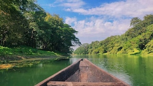 A wooden boat on a calm river surrounded by lush greenery. - Resort Ichche Kuthi by Urban Express (Bangaon)