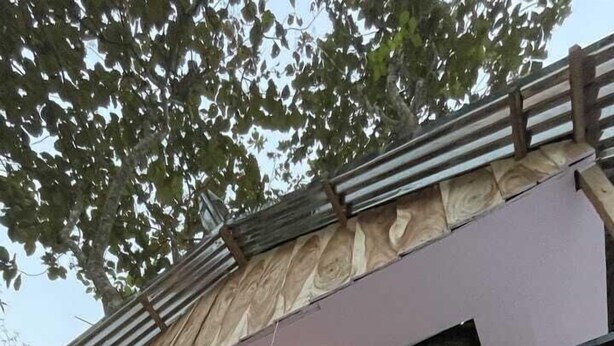 A wooden deck with a metal railing, a staircase, and a view of a building with a green door. - Resort Ichche Kuthi by Urban Express (Bangaon)