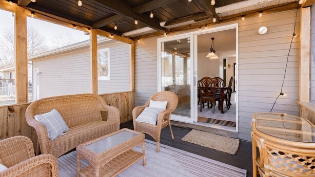 Un patio techado al aire libre con mobiliario de mimbre, una puerta de vidrio que da a un comedor interior y un techo de madera.