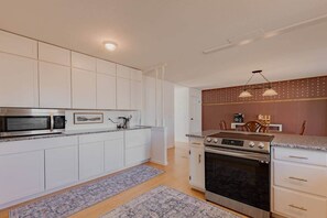 Une cuisine moderne avec des meubles blancs, un four à micro-ondes encastré, une cuisinière et un coin repas comprenant une table et des chaises.