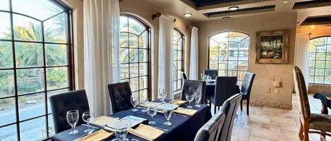 Un comedor con una mesa larga dispuesta para una comida, ventanas amplias y un techo decorativo.