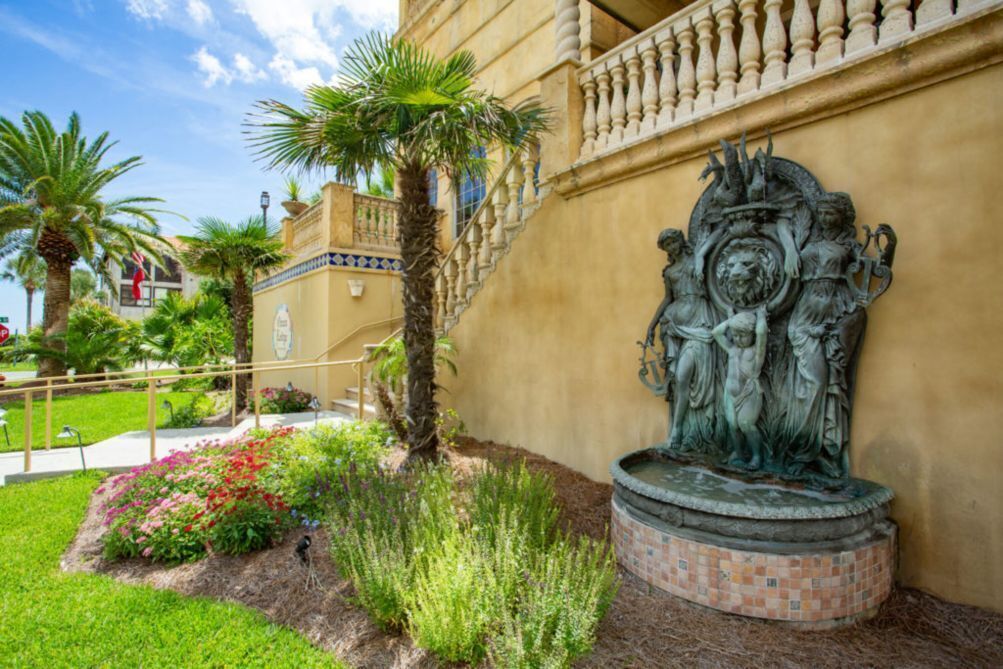 A statue of a historical figure on a pedestal, surrounded by a landscaped garden with palm trees and flowering plants.