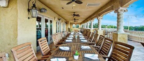 A covered outdoor dining area with wooden tables and chairs, ceiling fans, and a view of the water.