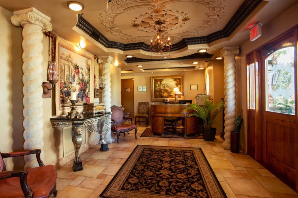 A lobby with a chandelier, ornate columns, a reception desk, and a large rug.