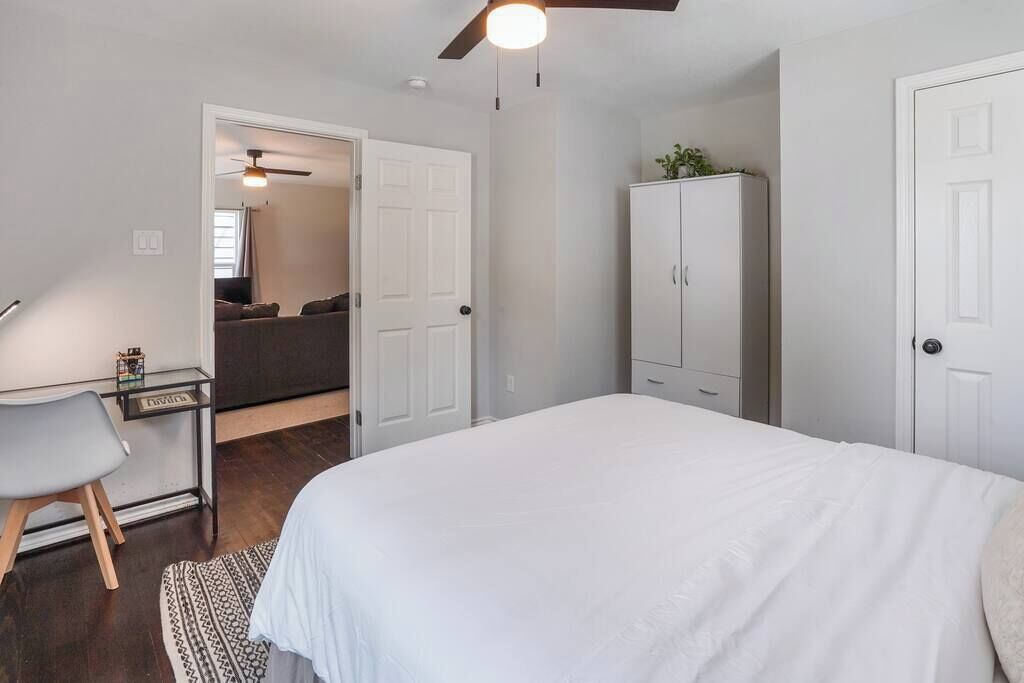 A bedroom with a bed, a desk, a chair, a wardrobe, and a ceiling fan.