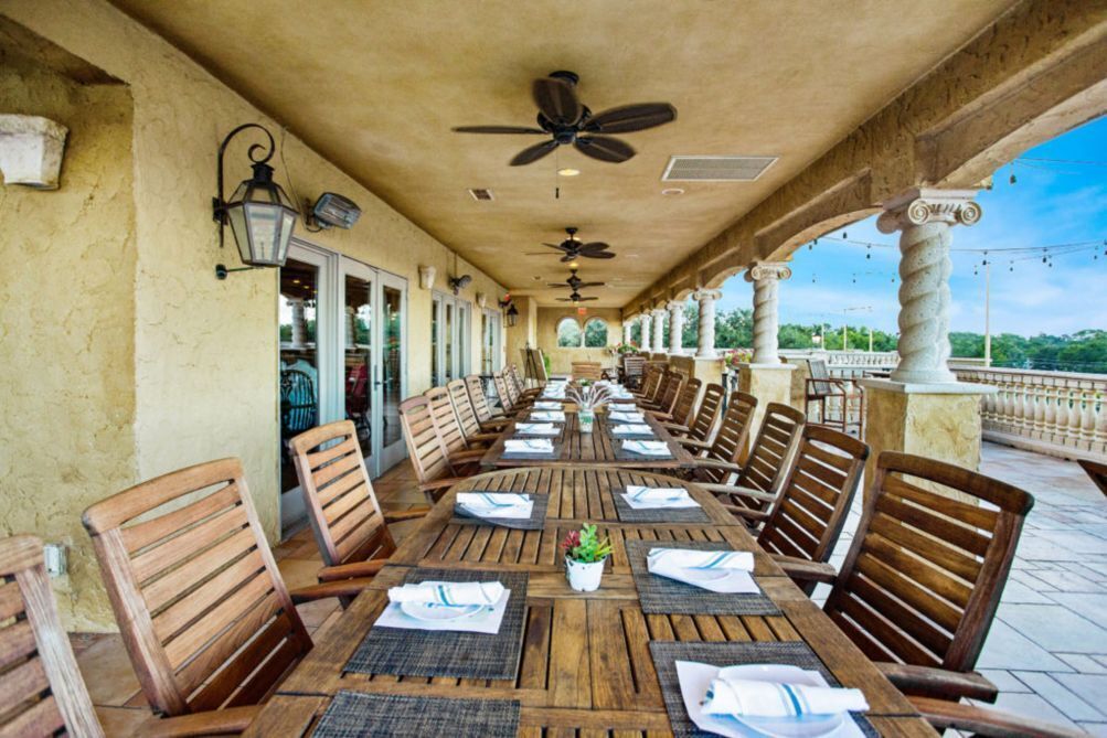 Un'area pranzo all'aperto coperta, con tavoli e sedie in legno, ventilatori a soffitto e vista sull'acqua.