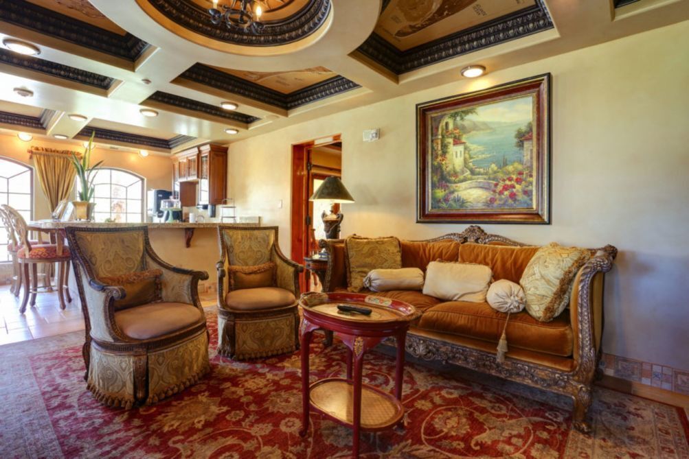 A spacious living room with ornate furniture, a large painting, and a red patterned carpet.