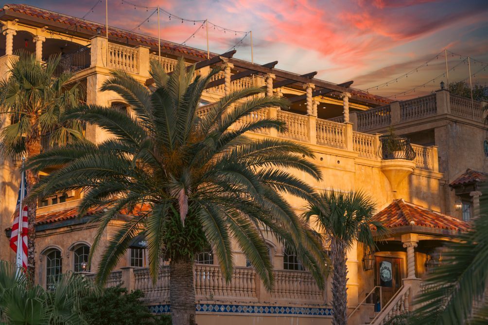 A historic building with a balcony, palm trees, and a flag.