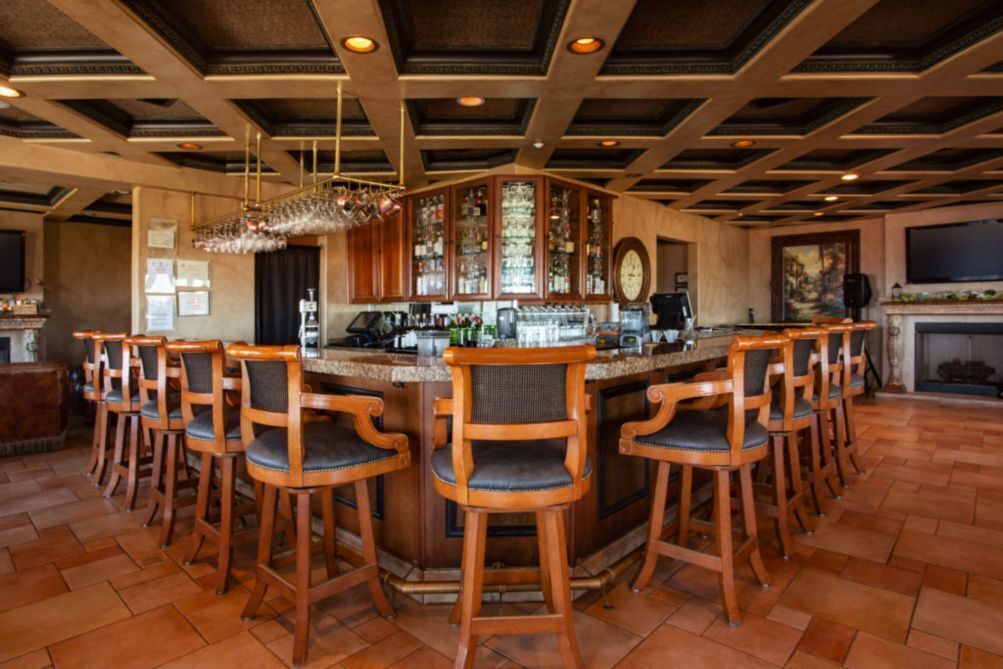 A bar area with a high ceiling, bar stools, a bar counter, and a large window.
