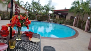 A poolside area with a table set for dining, a vase of flowers, and a clear blue pool. - Budget Inn Anaheim (Anaheim)