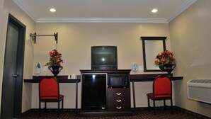 A compact hotel room with a kitchenette, two red chairs, a small TV, and decorative flowers. - Budget Inn Anaheim (Anaheim)