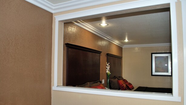 A room with a large window, a dark wooden door, a framed picture on the wall, and a vase with flowers on the windowsill. - Budget Inn Anaheim (Anaheim)