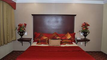 A bedroom with a large bed, red bedding, and two nightstands with flower vases.