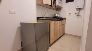 A compact kitchen with a refrigerator, microwave, and wooden cabinets. - Aparta Estudio Para Nómadas Digitales en Laureles (Medellín)