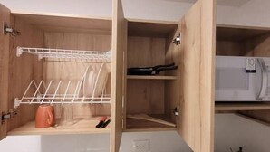 A wooden cabinet with a drying rack, a microwave, and a shelf with a kettle. - Aparta Estudio Para Nómadas Digitales en Laureles (Medellín)