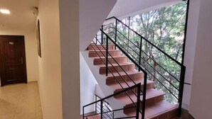 Un corridoio con una porta in legno e una scala con ringhiere in metallo che conduce verso un'area esterna.