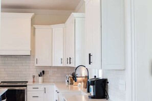 A modern kitchen with white cabinetry, a brick backsplash, and a coffee machine.